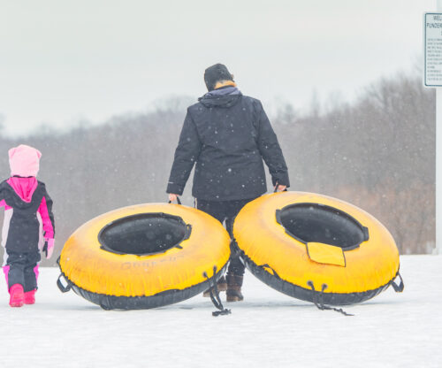 father and daughter carrying snow tubes